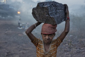 A young boy carries a chunk of coal into the mining camp where he lives.
